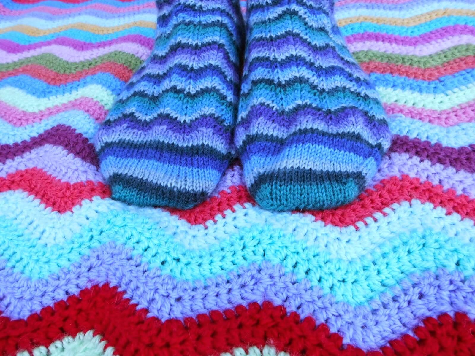 A pair of Neat Ripple Socks modelled on feet. The model is standing on a Neat Ripple blanket