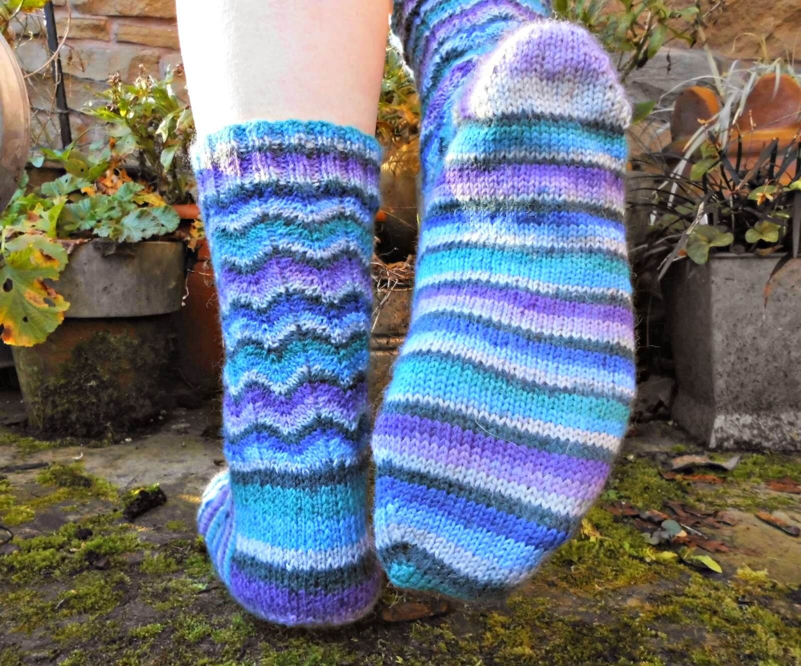A photo showing the sole of the Neat Ripple Socks. The model is standing on a mossy stone with one foot raised to show the sole to the camera