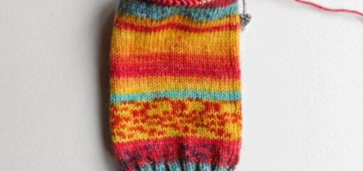 The leg and cuff of a striped yellow, orange and turquoise sock on a short circular needle