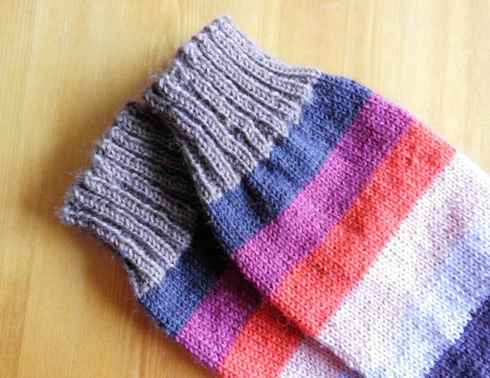 A pair of striped socks in shades of coffee, blue, purple, orange and beige on a wooden table.
