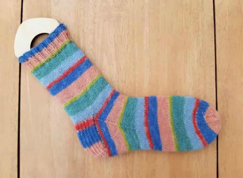 Image shows a finished stripy sock on a sock blocker lying on a wooden table