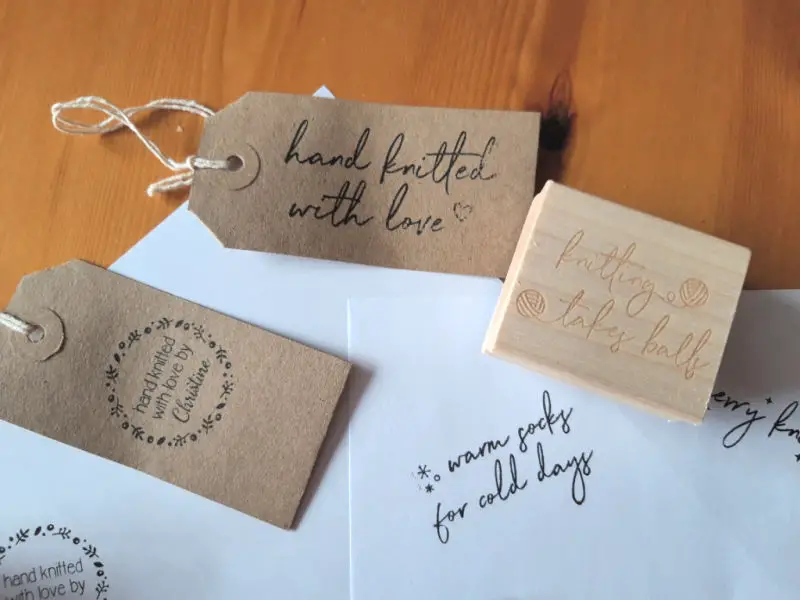 Brown luggage labels with stamped logos on them, and a piece of paper with stamps on it where Christine has tried out the ink stamps in the box