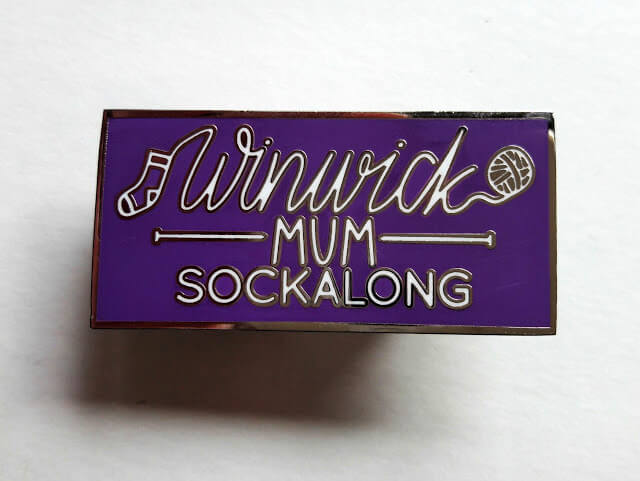 A purple pin badge with Winwick Mum Sockalong engraved on it in silver