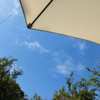 A blue sky with wispy clouds is visible between green tree tops and a cream sun parasol