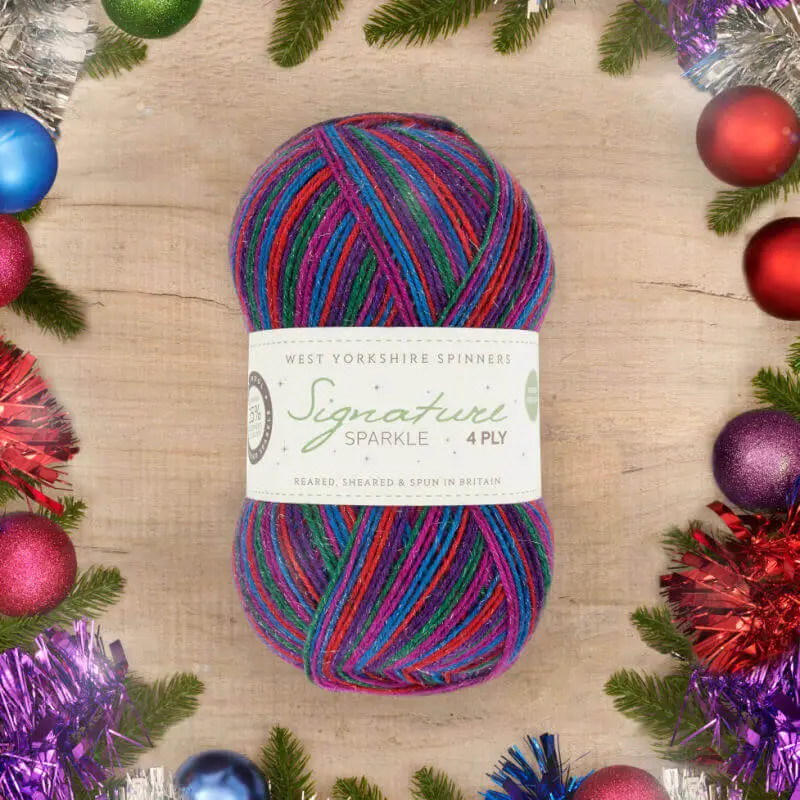 A ball of sparkly yarn in stripes of blue, green, pink, red and purple surrounded by a festive wreath of greenery and coloured baubles.