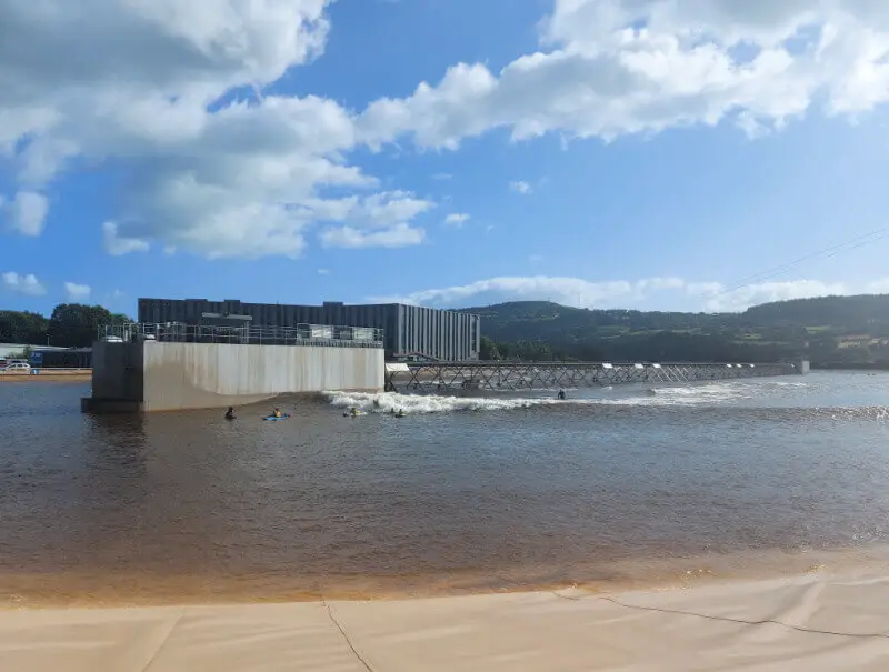 A view across the lagoon at Adventure Parc Snowdonia. In the centre is the wave machine which runs between concrete pontoons and in the background is a hotel.