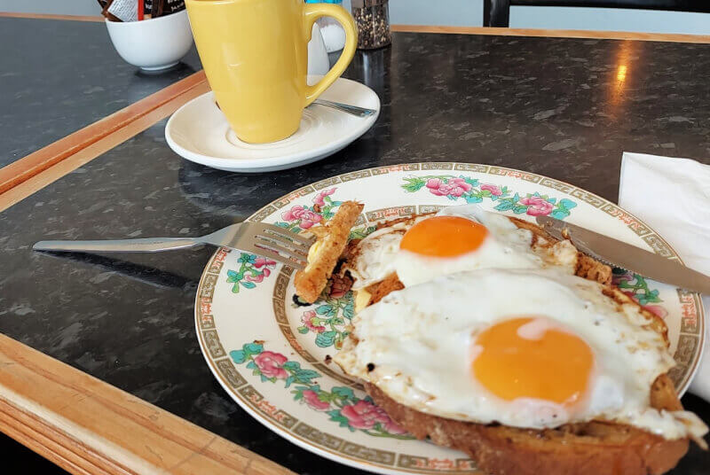Two fried eggs on toast on an Indian Tree-patterned plate. In the background is a yellow mug of tea.