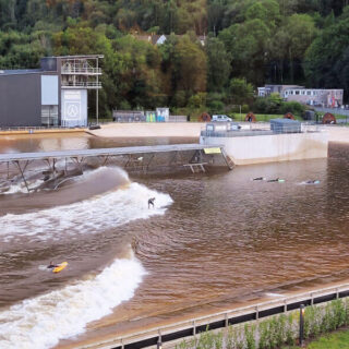 The surfing wave is half way across the photo now, the surfer is riding the wave and the beginners are still waiting!
