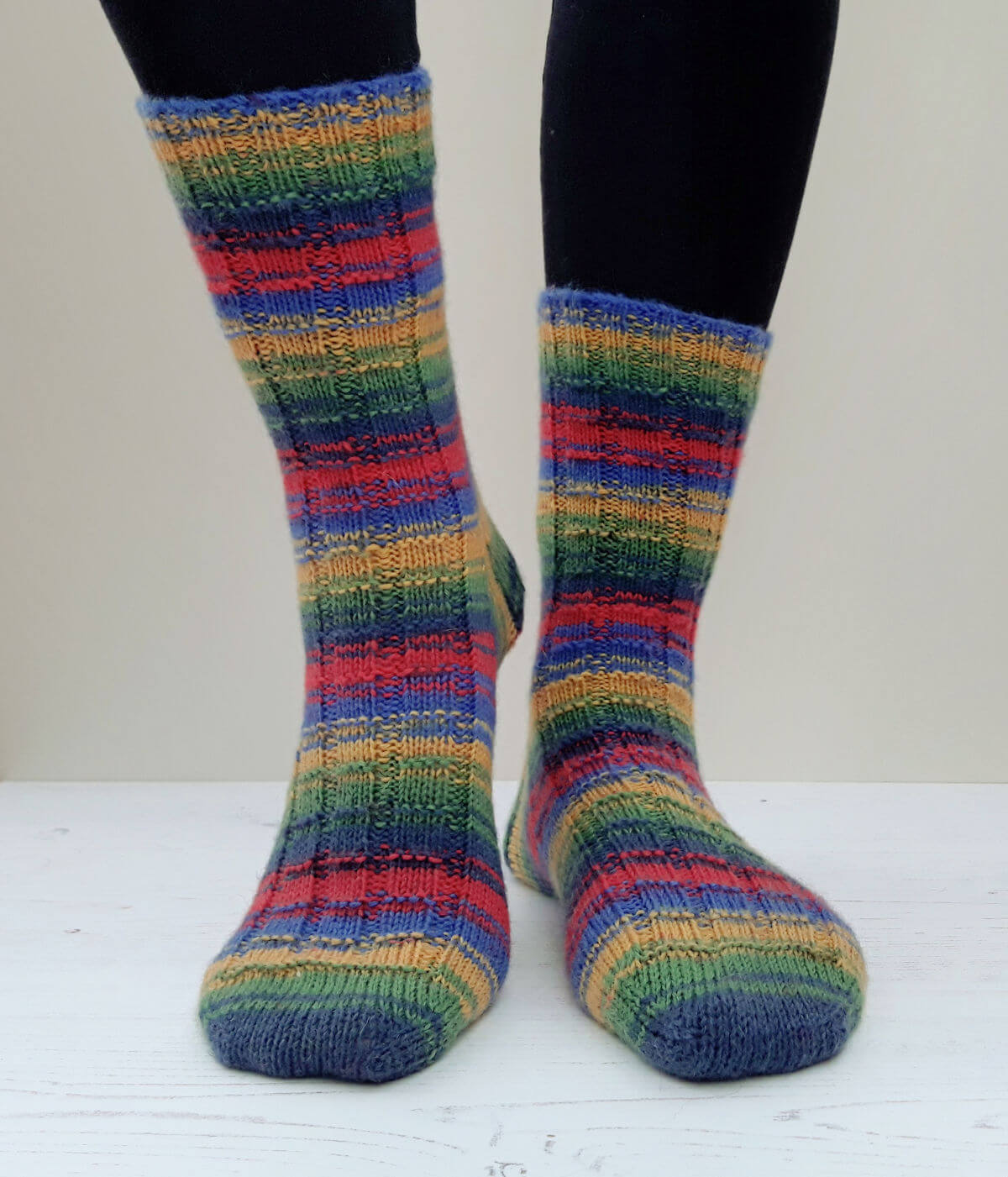 A pair of blue, green, yellow and red socks modelled against a cream background. One heel is slightly raised.
