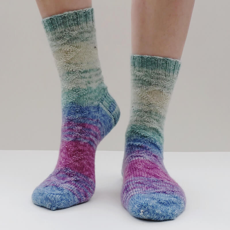 A pair of blue, green, yellow and purple socks modelled against a cream background. One heel is slightly raised.
