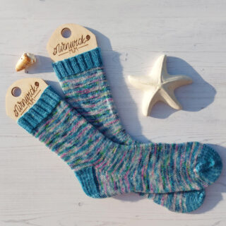 A pair of blue variegated socks on wooden sock blockers against a white wooden board background. There is a shell and a ceramic starfish next to the socks.
