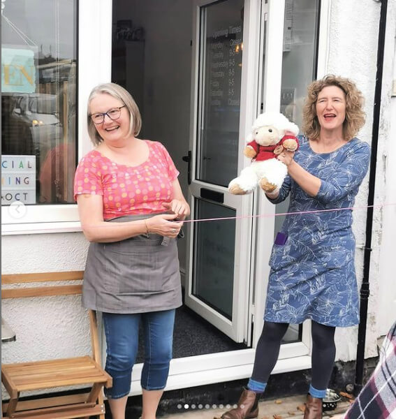Christine is holding a white toy sheep in a red jumper up and Diane is laughing.