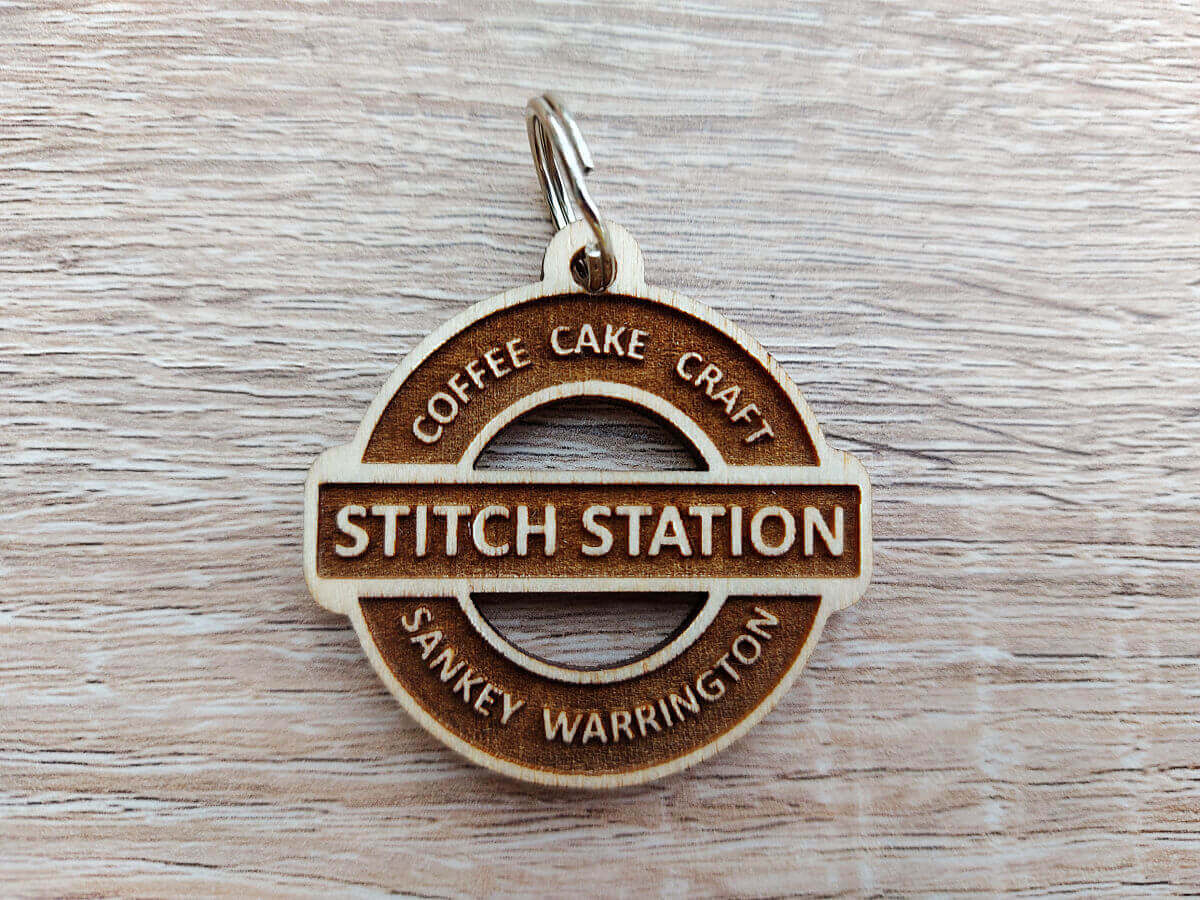 A wooden keyring in the shape of a railway station sign with the Stitch Station logo etched onto it.