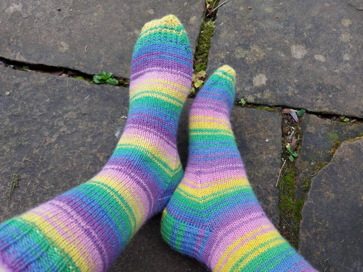 Christine is wearing her new Wildflower socks and wiggling her toes! The socks are pictured against a damp stone flag background.