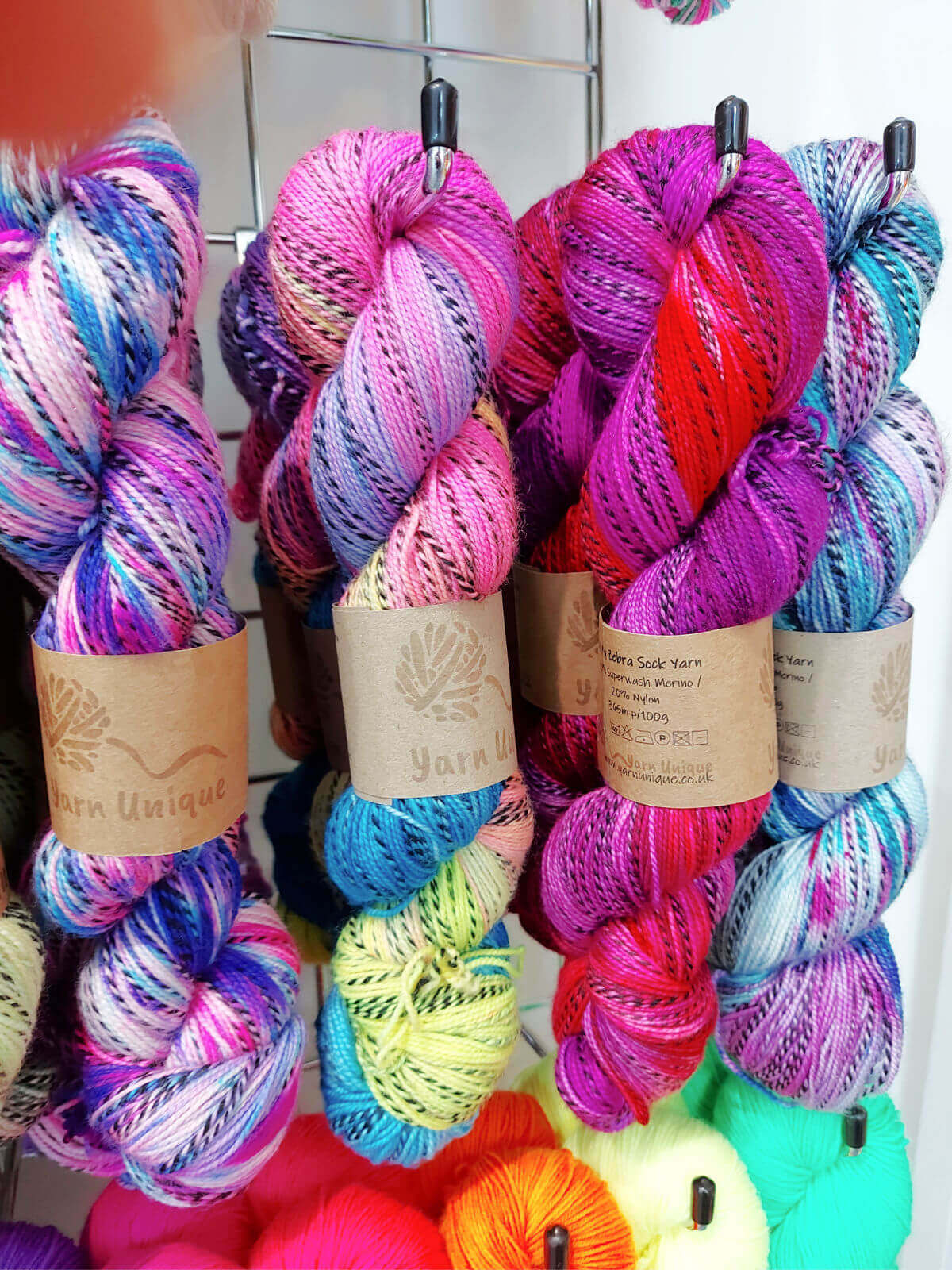 Large skeins of multi-coloured yarn with a black fleck running through them hang from a rack.
