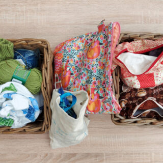 Two wicker baskets on a pale wooden table. Each contains brightly coloured project bags. There are more project bags between the baskets.