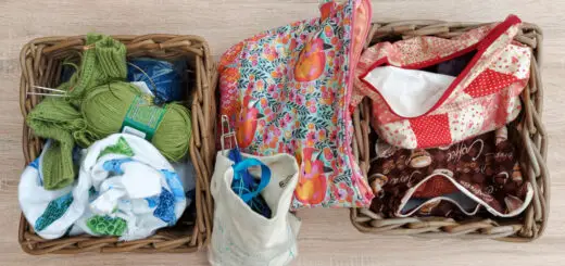 Two wicker baskets on a pale wooden table. Each contains brightly coloured project bags. There are more project bags between the baskets.