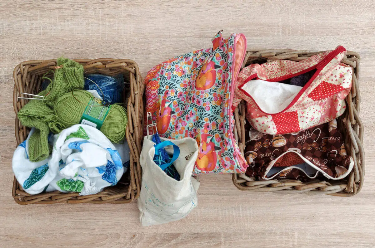 Two wicker baskets on a pale wooden table.  Each contains brightly coloured project bags.  There are more project bags between the baskets.