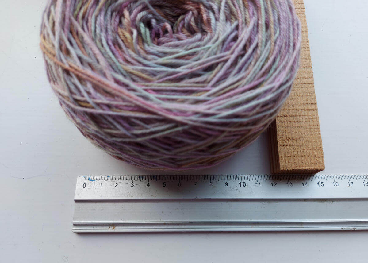 The yarn cake sits against a metal ruler and a piece of wood shows where the edge of the cake reaches to - 12 cm