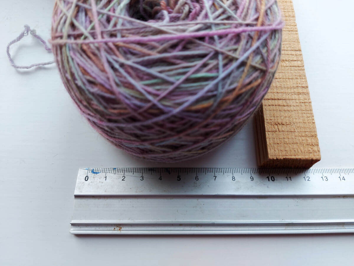 The yarn cake sits against a metal ruler and a piece of wood shows where the edge of the cake reaches to - 9.5cm
