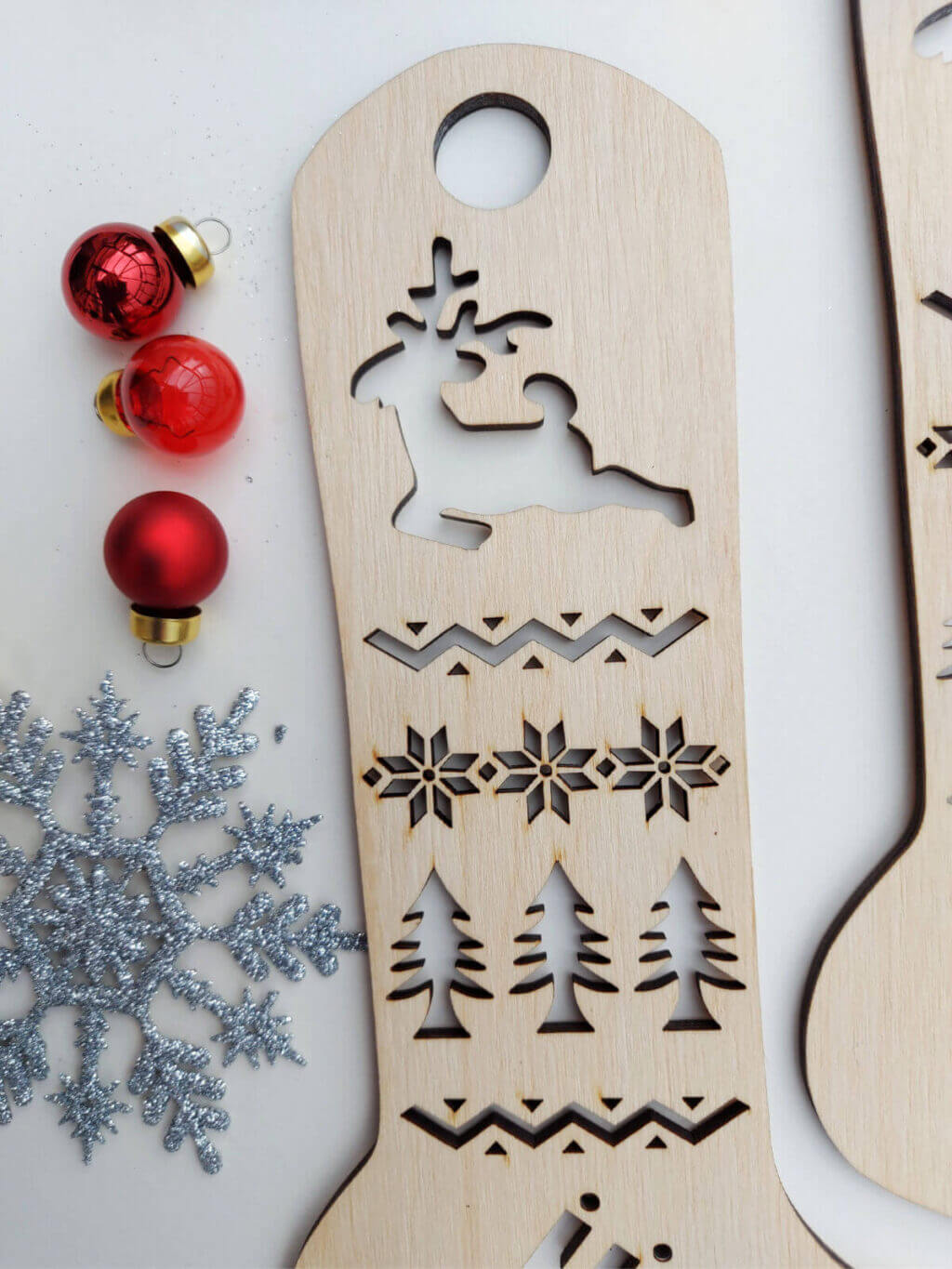 A close up of the leg section of a wooden sock blocker. At the top is a cutout of a reindeer with festive shapes and Christmas trees underneath.