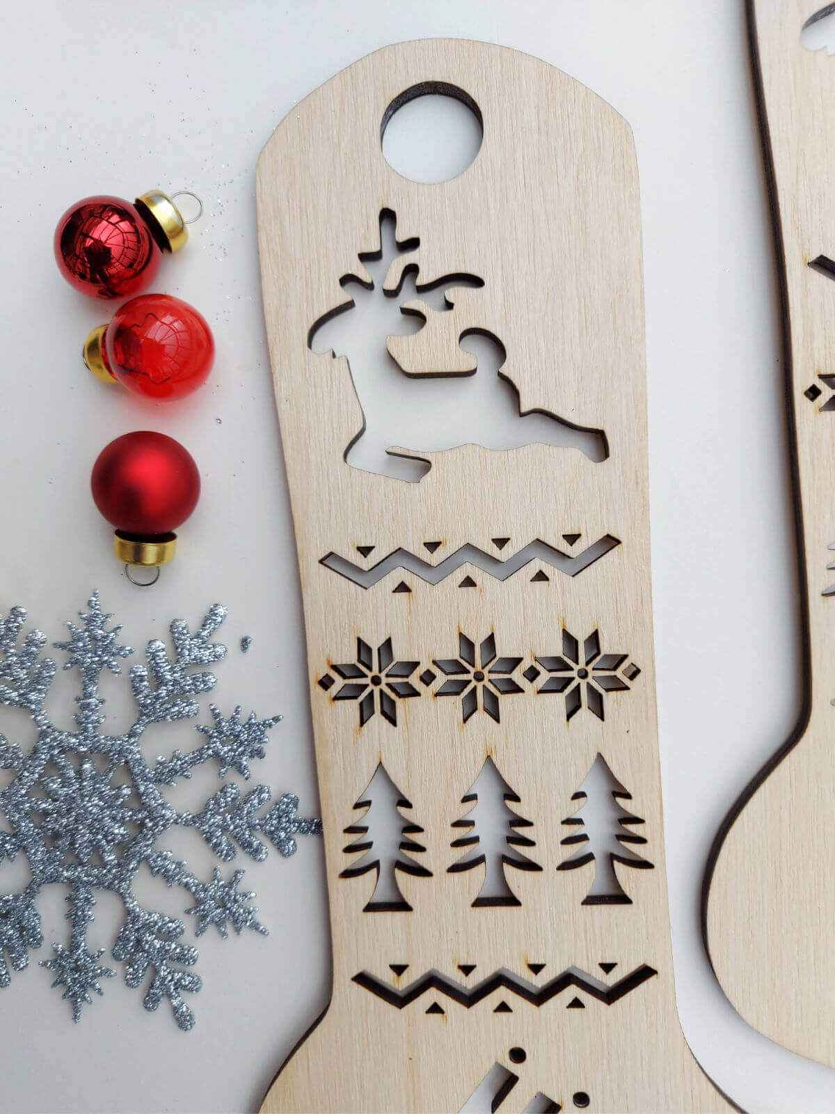A close up of the leg section of a wooden sock blocker. At the top is a cutout of a reindeer with festive shapes and Christmas trees underneath.