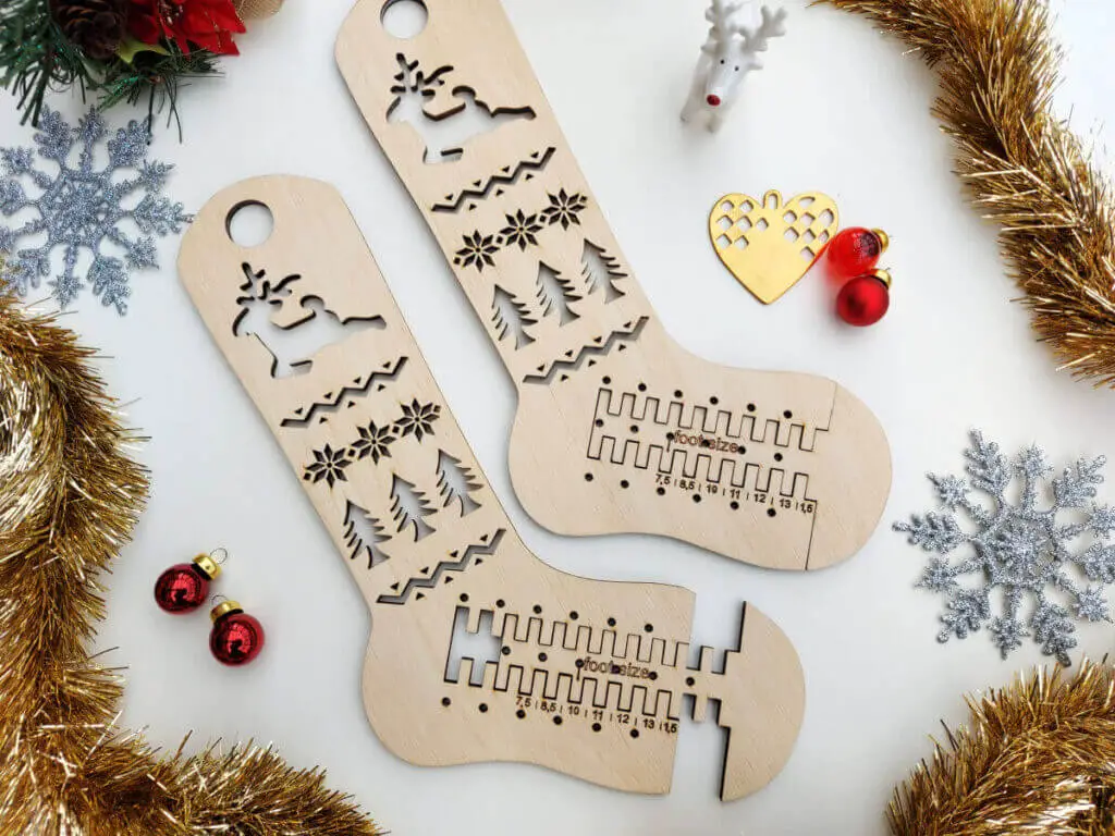 A flatlay of adjustable wooden sock blockers surrounded by Christmas stars, red glass baubles, gold tinsel and a tiny ceramic reindeer. 