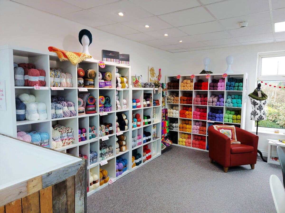 Shelving units containing brightly coloured balls of yarn with a red leather club chair to the right.