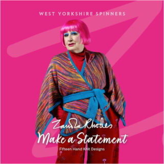 Dame Zandra Rhodes stands against a pink background that matches the colour of her hair. She is wearing a hand knitted wrap cardigan in shades of pink and blue.