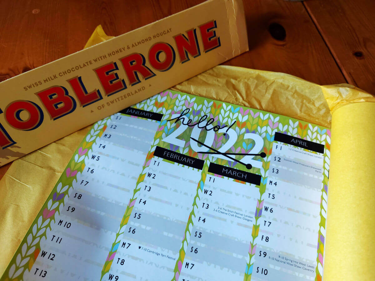 A 2022 year planner held down by a Toblerone on the left and still rolled in yellow tissue paper on the right