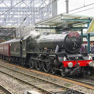 A green steam train standing at a station with people waiting to get on