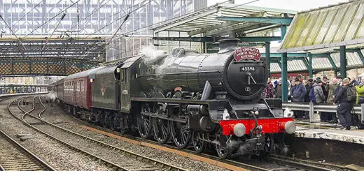A green steam train standing at a station with people waiting to get on