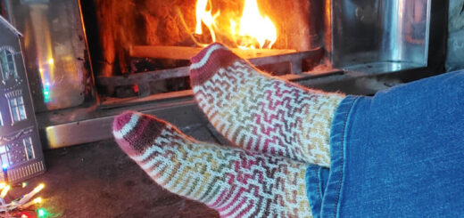 A pair of feet wearing a pair of mosic patterned socks stretched out on a hearth by an open fire. Th