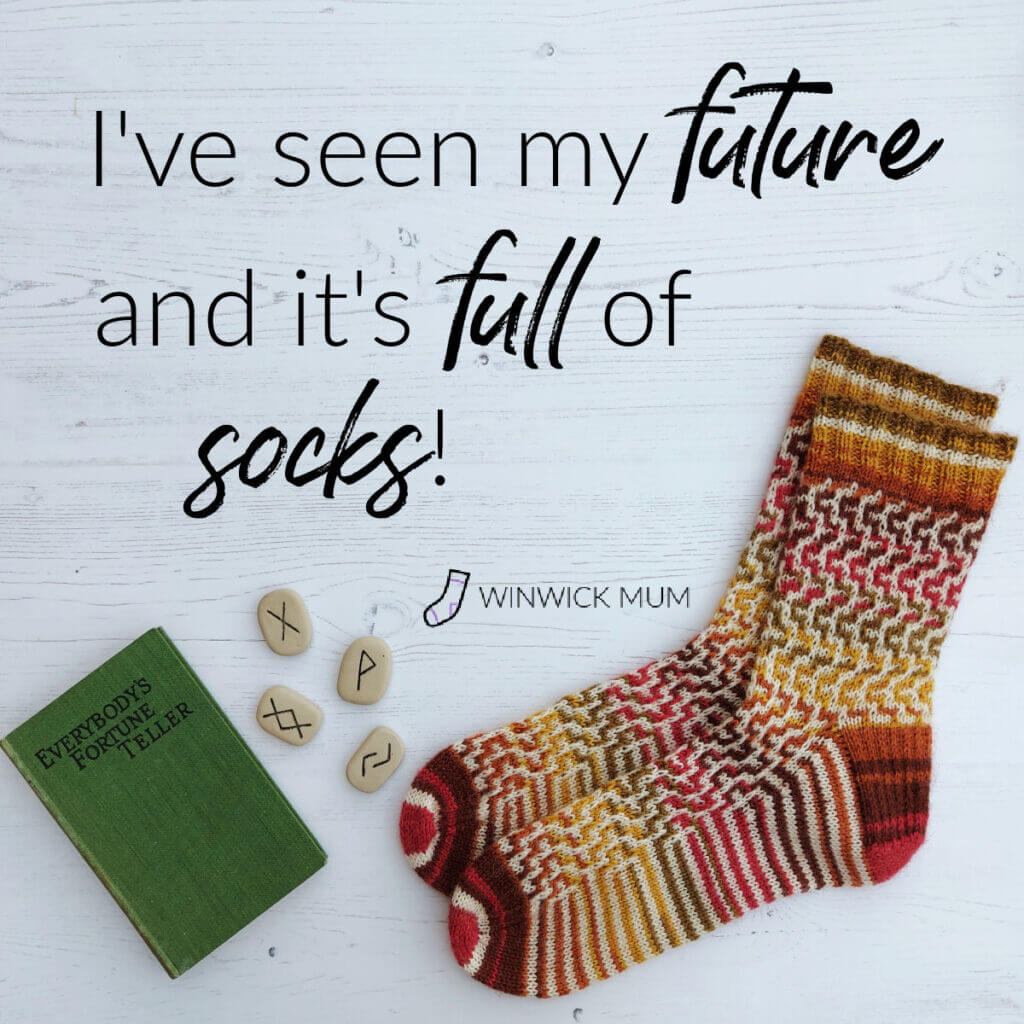 A pair of socks in shades of red, brown, green and yellow with a white pattern working its way down the socks are lying on a white wooden floor. To the left is a vintage book with a green cover entitled "Everybody's Fortune Teller" and there are four Rune stones lying next to it. The words on the photo read "I've seen my future and it's full of socks!"