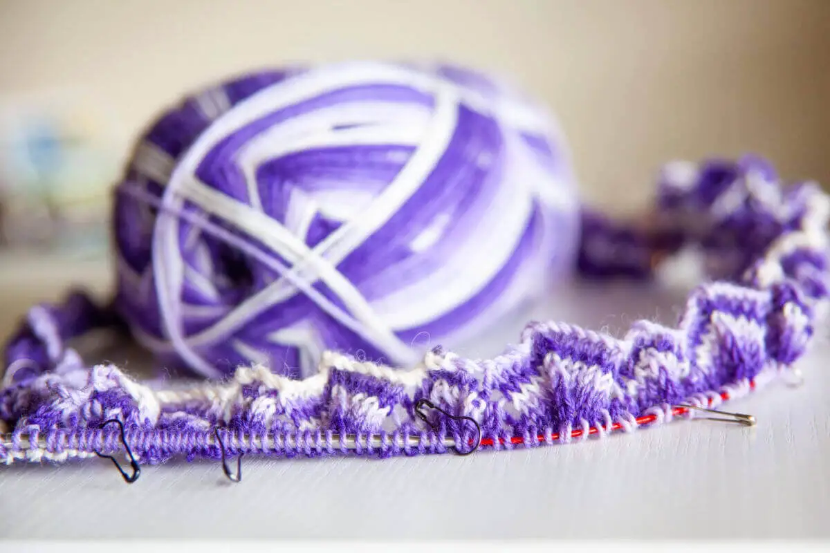 A ball of purple and white striped yarn is sitting within a circle of knitting