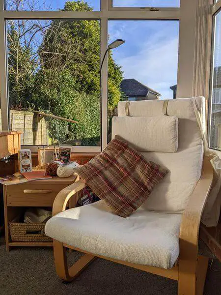 A wooden-framed armchair with white seat pads in front of a window. It's a bright, sunny day.