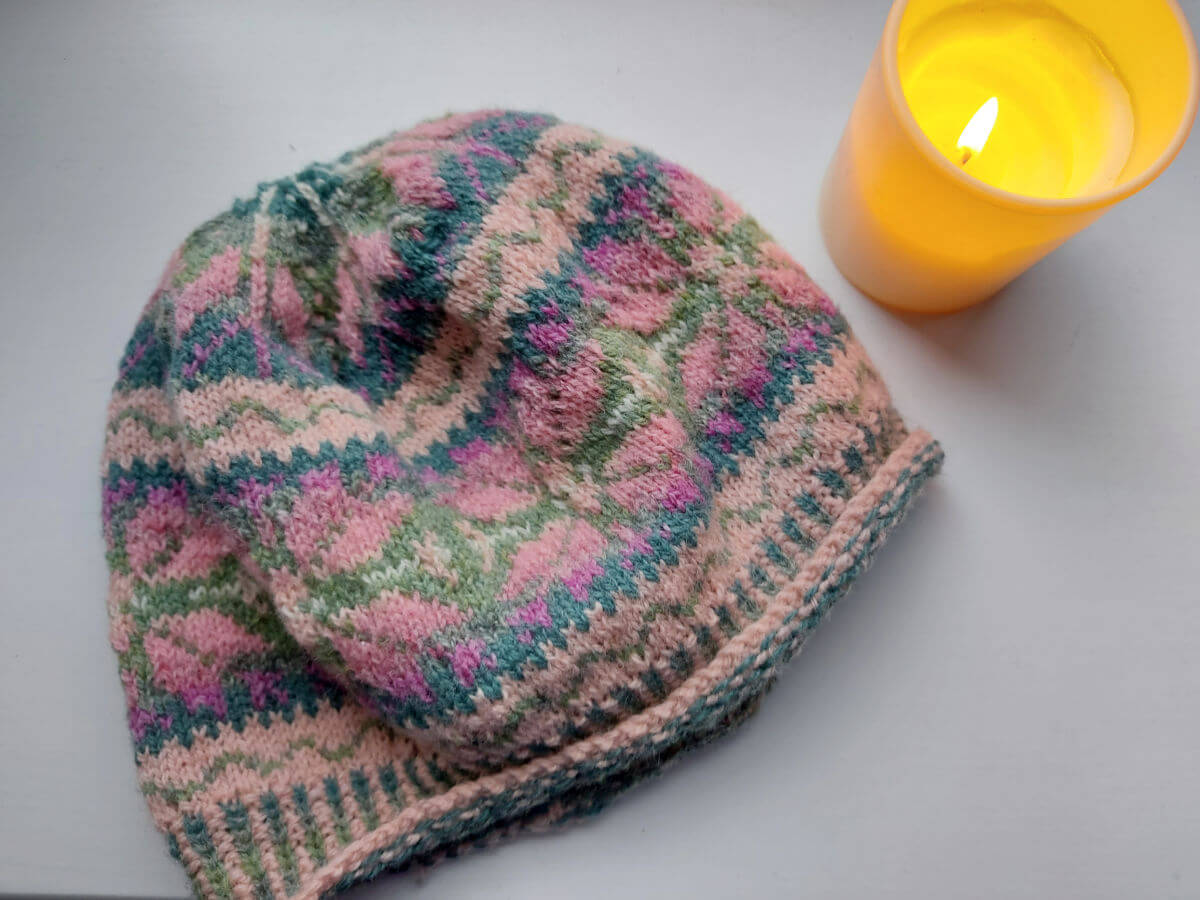 A colourwork hat and a candle on a white background
