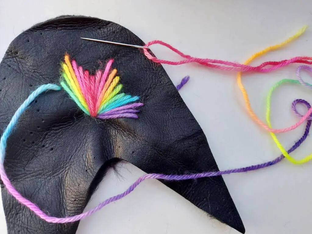 A rainbow star pattern is being stitched onto the leather upper of a slipper