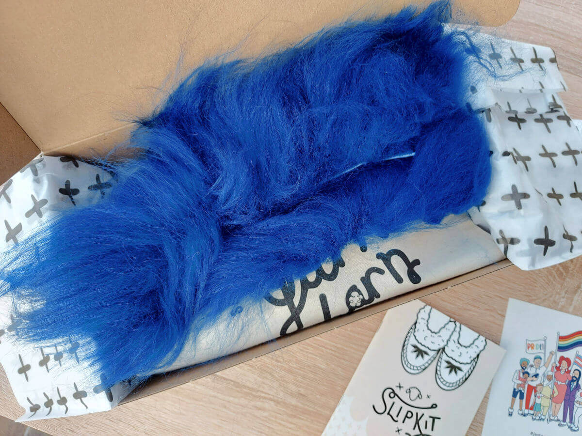 Bright blue sheepskin strips lie across the contents of a slipper kit in a cardboard box