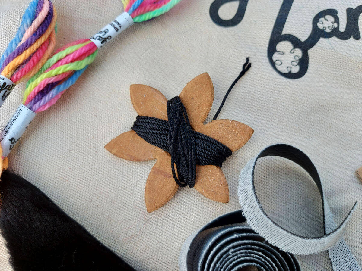 A cardboard flower with black thread wrapped around it lies on a fabric bag
