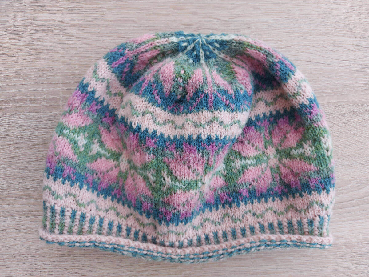 A knitted colourwork hat lies on a wooden table