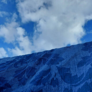 A blue patterned duvet cover on a washing line against a blue and white cloud sky