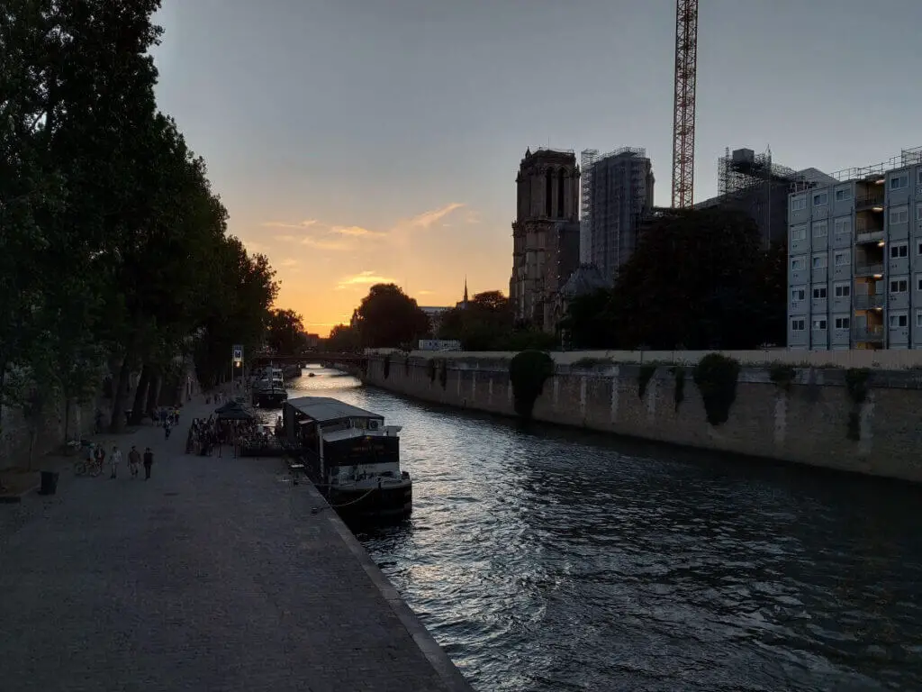The river Seine with the Notre Dame cathedral on the bank the right. The sun is setting and the sky is pink