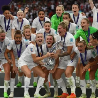 The England women's football team, all in white kit apart from the goalie in bright green, celebrate winning the Euros