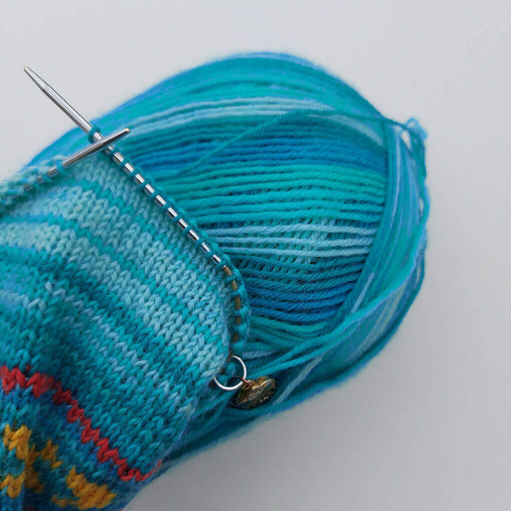 A partly-knitted socks sits on a ball of turquoise stripy yarn