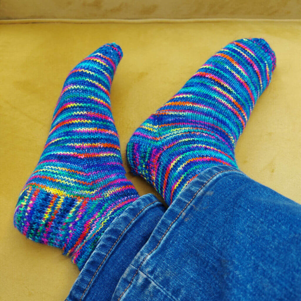 Christine is wearing a pair of blue jeans and pair of blue and rainbow socks. She is sitting on a mustard-coloured sofa