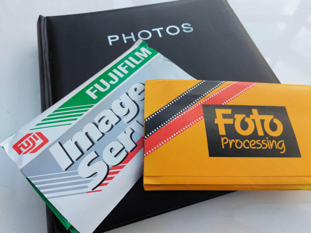 Two packets of photos from photo developers sit on a black photo album. All are lying on a white high-gloss table.