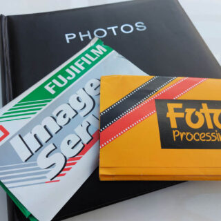 Two packets of photos from photo developers sit on a black photo album. All are lying on a white high-gloss table.