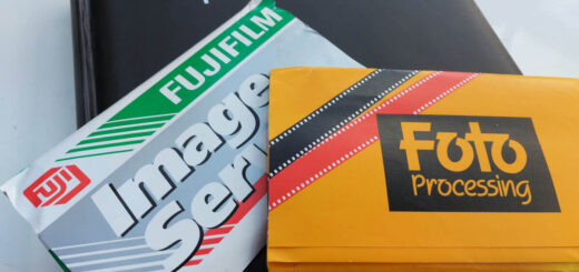 Two packets of photos from photo developers sit on a black photo album. All are lying on a white high-gloss table.