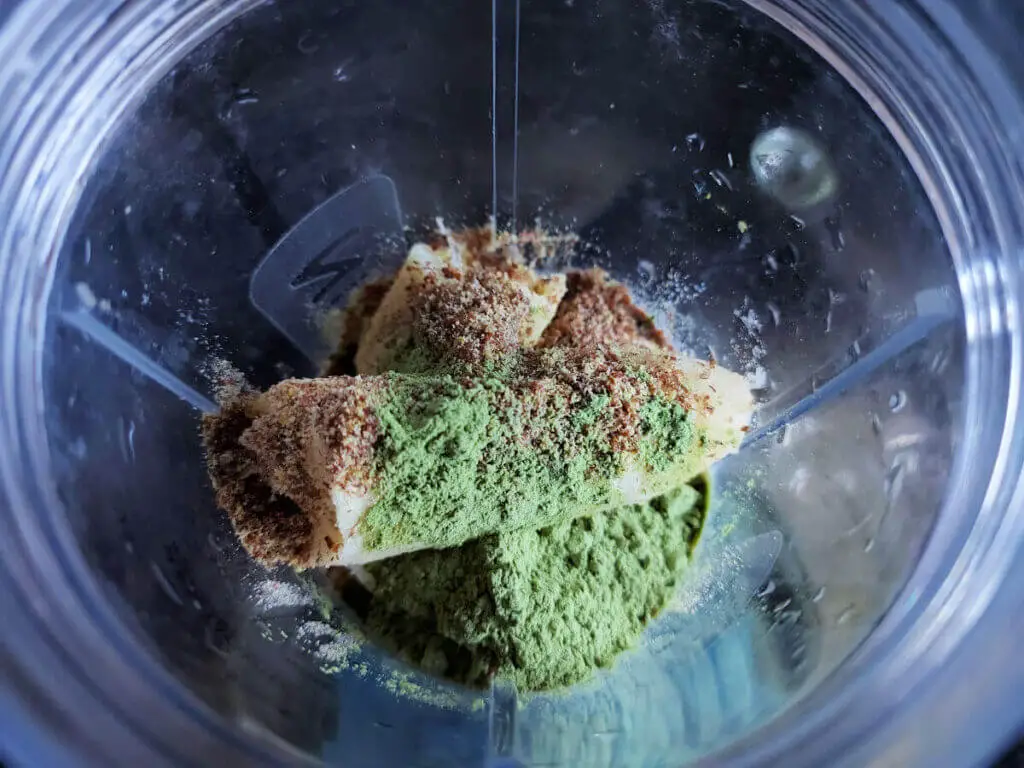 A banana, ground linseed and green barley grass powder in a blender cup